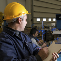 Trabajador tomando notas con un casco amarillo.