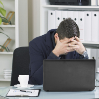 Un hombre en su trabajo tapándose la cara y mirando hacia abajo.